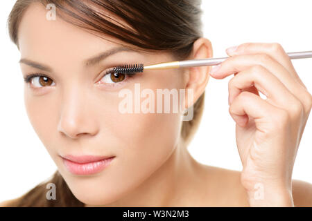 Mascara woman putting makeup on eyes. Asian female model face closeup with eye brush on eyelashes. Stock Photo