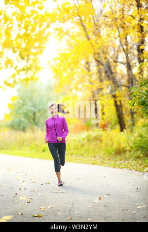 Autumn lifestyle woman running in fall forest with beautiful yellow leaves foliage. Full length portrait of runner jogging outdoor on forest road. Mixed race Asian Caucasian girl in her 20s. Stock Photo