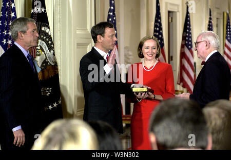 Washington, DC - September 29, 2005 -- Friends and family stand up as John Glover Roberts, Jr., center left, is sworn-in as the 17th Chief Justice of the United States by Associate Justice John Paul Stevens, right, in the East Room of the White House in Washington, DC on September 29, 2005. His wife, Jane Sullivan Roberts, center right, holds the bible. United States President George W. Bush looks on from left.Credit: Ron Sachs/CNP | usage worldwide Stock Photo