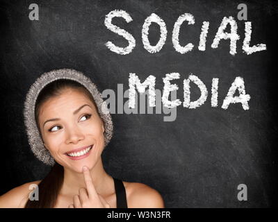 Social media concept with university student looking thinking at SOCIAL MEDIA text on blackboard. Female college student girl in front of black chalkboard. Trendy cool multiracial asian caucasian girl Stock Photo