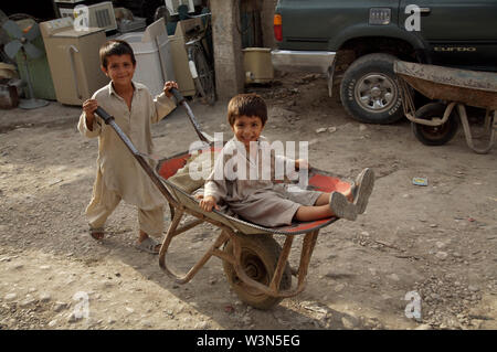 A young boy wheels his younger brother on a cart. They work as porter, at the main market, in the city of Mazar-e-Sharif, in the northern province of Balkh. An estimated 60,000 children have fled broken families, poverty and conflict, and now live or work in the streets of major cities. Afghanistan. June 26, 2007. Stock Photo