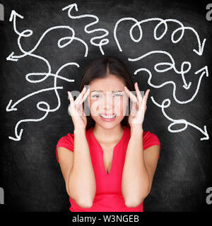 Confused woman - people feeling confusion and chaos. Indecisive, disorientated and bewildered woman stressed with headache over decision making. Girl in 20s on blackboard background. Asian / Caucasian Stock Photo