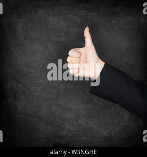 Thumbs up hand on blackboard / chalkboard background. Woman hand sign of approval and succes. Teacher or female student concept image. Black blackboard texture background icon. Stock Photo