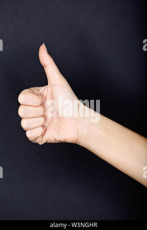 Thumbs up close up on black background. Female hand giving like hand sign thumbs up approval gesture. Stock Photo