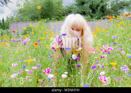 Blonde middle aged woman in her backyard full of wildflowers. Lawn replacement. Stock Photo