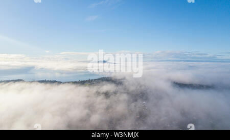 Aerial drone shot flying above the cloud, looking at the summit of Rangitoto Island. Stock Photo