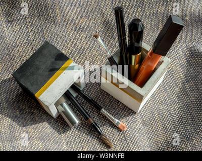 Cosmetic tools set in cubic shape concrete container on sackcloth background. Stock Photo