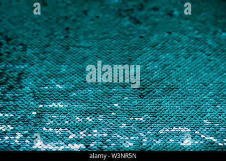 Shiny iridescent turquoise sequins on fabric. Abstract festive sparkling background. Stock Photo