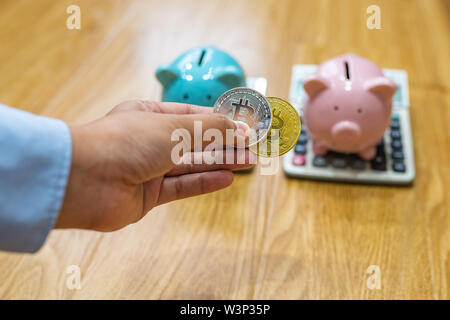Woman hand holding two bitcoins in front of piggybank Stock Photo