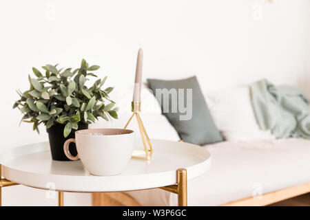 The interior of the room in the Scandinavian style. A cup of coffee on the coffee table next to the candles and a potted plant Stock Photo