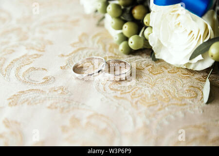 wedding rings lie on the fabric next to a bunch of flowers Stock Photo