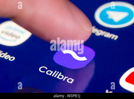 Finger pressing icon to load Facebook's Calibra Digital Wallet app on a mobile device to send & receive money using Libra blockchain cryptocurrency. Stock Photo