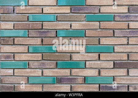 light and dark brown brick wall with a few green colored bricks in it Stock Photo