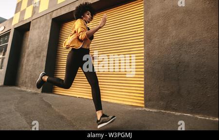 Sporty young woman running on sidewalk in morning. Health conscious female sprinting outdoors. Stock Photo
