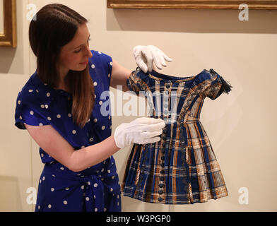 A Royal Collection employee handles a dress worn by Albert Edward, Prince of Wales, between the years 1844-46, on display at the exhibition to mark the 200th anniversary of the birth of Queen Victoria for the Summer Opening of Buckingham Palace, London. Stock Photo