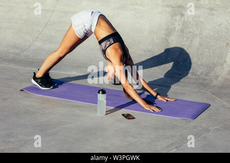 Healthy woman doing yoga in morning. Female in sportswear doing stretching workout outdoors, she is practicing downward facing dog yoga pose. Stock Photo