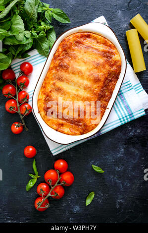 Stuffed cannelloni with bechamel sauce. Cannelloni pasta baked with meat, cream sauce, cheese on a black background. Top view, flat lay. Stock Photo