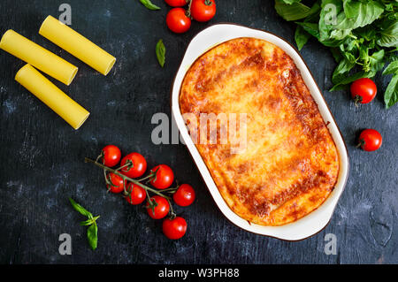 Stuffed cannelloni with bechamel sauce. Cannelloni pasta baked with meat, cream sauce, cheese on a black background. Top view, flat lay. Stock Photo