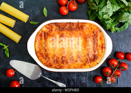 Stuffed cannelloni with bechamel sauce. Cannelloni pasta baked with meat, cream sauce, cheese on a black background. Top view, flat lay. Stock Photo