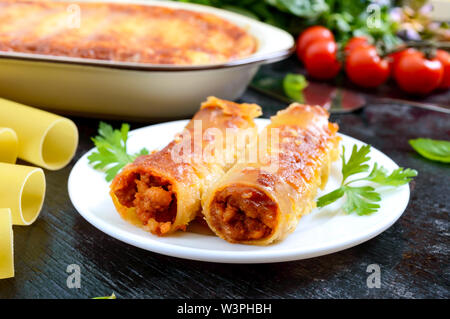 Stuffed cannelloni with bechamel sauce. Cannelloni pasta baked with meat, cream sauce, cheese on a black background Stock Photo