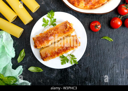Stuffed cannelloni with bechamel sauce. Cannelloni pasta baked with meat, cream sauce, cheese on a black background. Top view, flat lay. Stock Photo