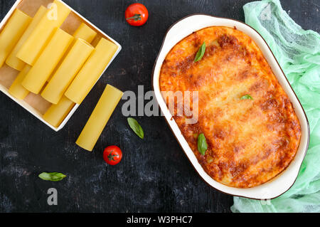 Stuffed cannelloni with bechamel sauce. Cannelloni pasta baked with meat, cream sauce, cheese on a black background. Top view, flat lay. Stock Photo