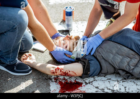 Ambluence workers applying emergency care to the injured bleeding man lying on the pedestrian crossing after the road accident Stock Photo
