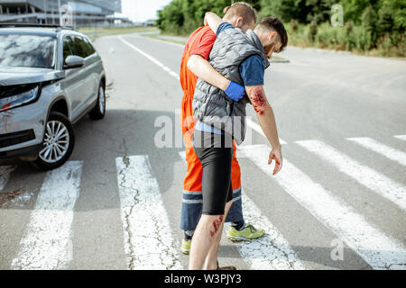 Medic in uniform helping injured man to walk, applying first aid after ...