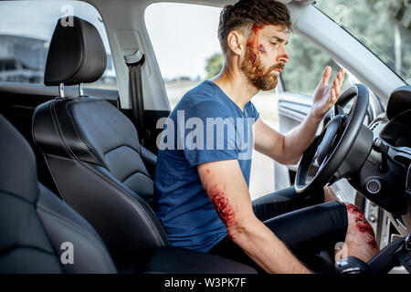 Fastened driver with deep bleeding injuries feeling shocked after the road accident inside the car Stock Photo