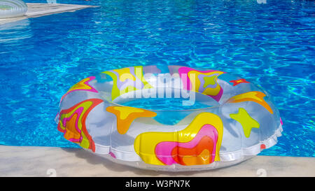 Vibrant rubber ring floating on the blue water of a swimming pool in the summer sunlight Stock Photo