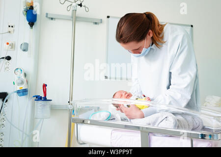 Female nurse with premature born baby in intensive care unit holding infant in her hands Stock Photo