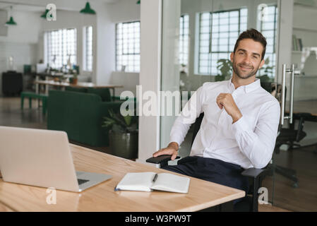 Smiling young businessman sitting at his desk in an office Stock Photo