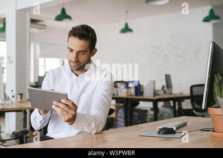 Young businessman sitting at his desk using a digital tablet Stock Photo