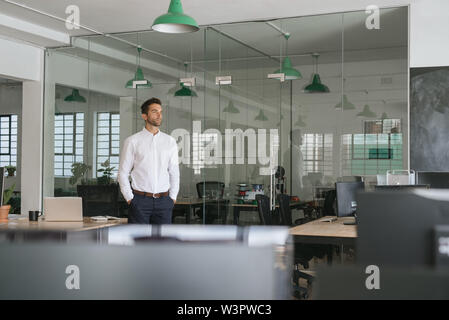 Young businessman standing in an office looking deep in thought Stock Photo
