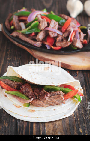 Beef steak fajita over a stack of tortilla wraps with cast iron pan of fresh hot fajita mix in the background.. Selective focus with blurred backgroun Stock Photo