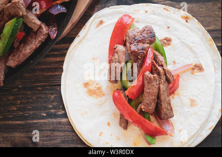 Beef steak fajita over a stack of tortilla wraps with cast iron pan of fresh hot fajita.. Image shot from top view. Stock Photo
