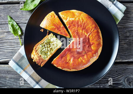 Green Bean spinach and blue cheese pie on a black plate on a rustic wooden table, horizontal view from above, flat lay, close-up Stock Photo