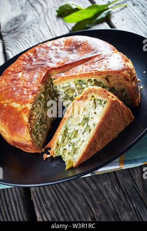 close-up of spinach Green Bean and blue cheese pie sliced on a black plate on a rustic wooden table, vertical view from above Stock Photo