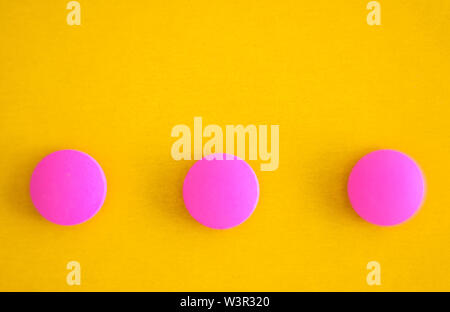 Composition of three pink round pills on a yellow background. Flat lay. Copy space. Trend Close-up. Stock Photo