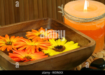Orange marigold flowers floating in wooden bowl, burning candle and stones. Spa still life Stock Photo