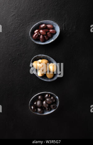 Various types of olives in bowls, shot from the top on a black background. Purple, green almond stuffed, and black pitted olives Stock Photo