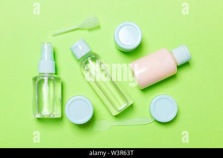 Set of travel size cosmetic bottles on green background. Flat lay of cream jars. Top view of bodycare style concept. Stock Photo