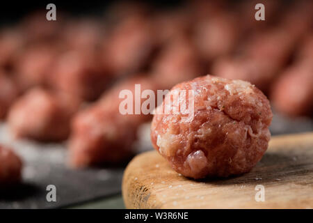 closeup of a raw meatball on a wooden chopping board placed on a table and some other meatballs in the background Stock Photo