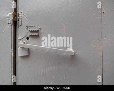 A fragment of a rough iron door with a mechanical combination lock painted with gray oil paint. There is a padlock on the door handle. Stock Photo
