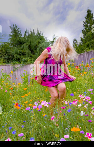 Blonde woman dancing in her backyard full of wildflowers. Stock Photo