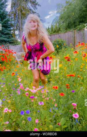 Blonde woman dancing in her backyard full of wildflowers. Stock Photo