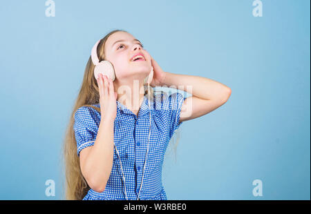 Inspired by music. Little kid listening music. Cute kid with headphones blue background. Small girl wearing stereo headphones. Child using technology for leisure or education. Modern headphones. Stock Photo