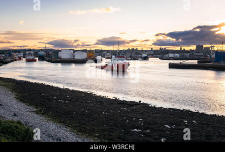 Ship leaving an industrail harbour with fuel tanks on the piers at sunset Stock Photo