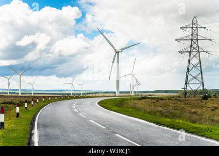 Country road through a wind turbins and high voltage pylons and cloudy sky Stock Photo