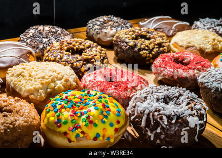 assorted donuts, some with bites missing, on wooden cutting board reflected in mirror Stock Photo